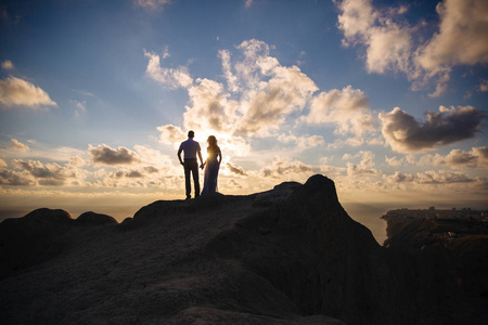 夕阳下一对相爱的情侣的剪影.男人在俯瞰大海的高山上拥抱一个女人.