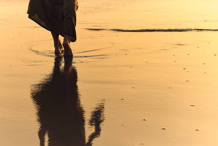 浪漫的少女赤脚在沙滩上漫步.日落时,女人光着脚在海里散步.