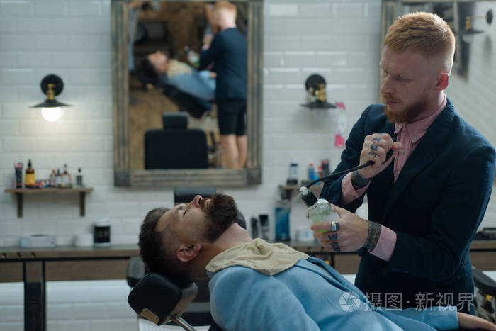 刮胡子的和剃须刀的.理发师在理发店为一个帅哥工作.
