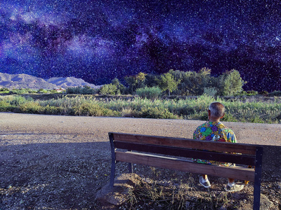 星星边一个男人坐在沙滩边的座位上观看第一颗夜空星星.照片