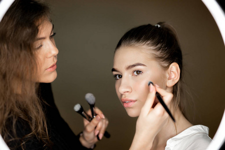 给人化妆化妆师那个迷人的女孩正在给一个漂亮的年轻女孩化妆照片