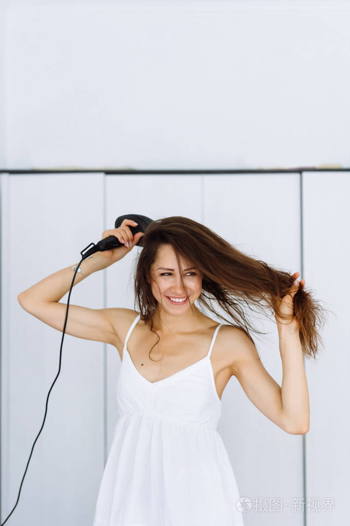 穿着浴袍的女人用白色背景的吹风机吹干头发