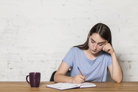 疲倦乏力疲倦的女孩在笔记本上写字.她坐在房间里的一张桌子旁.