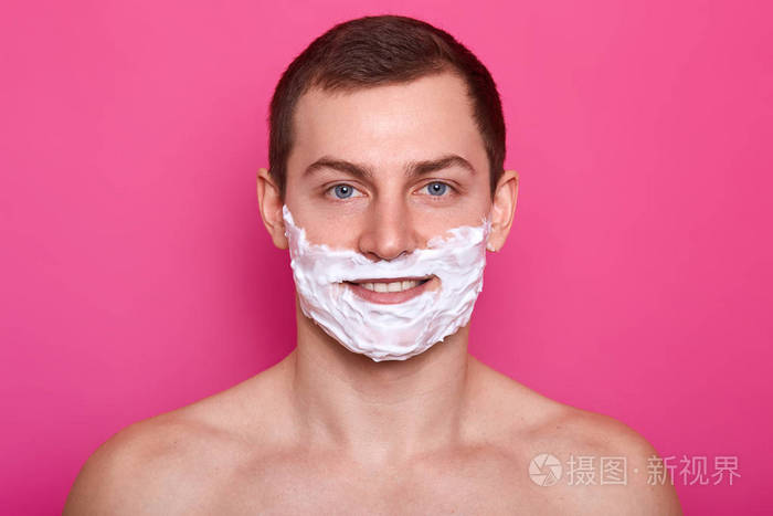 一张脸上有剃须泡沫的帅哥的特写照片背景为粉色男人在浴室刮胡子这个