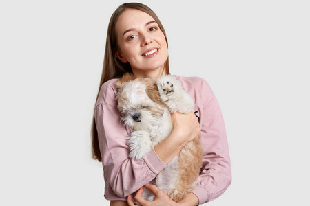 开朗的欧洲女模特手上抱着一只困倦的小狗,用狗粮玩耍和喂食,脸上露出