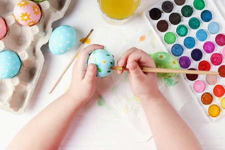 孩子手画复活节彩蛋,颜料和刷子在一张白色的桌子上.为假期做准备.