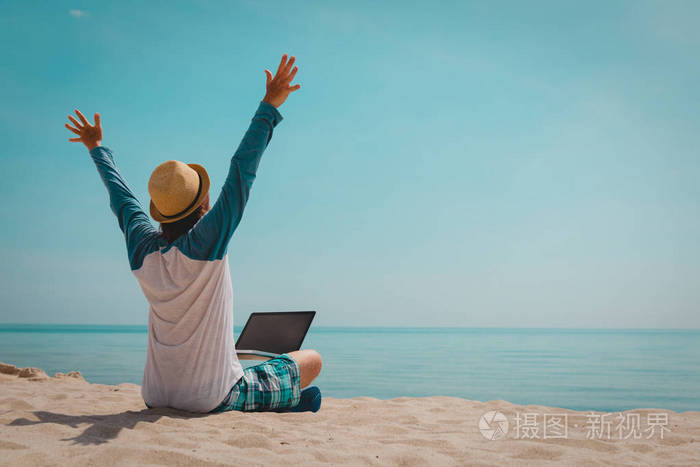 快乐的年轻人在海滩上用笔记本电脑工作