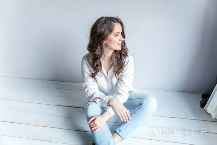 在明亮的房间里靠着白墙坐着的女孩