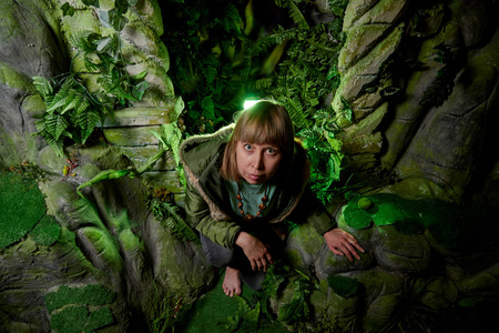 一个穿着绿色夹克,金发碧眼的女孩,在一块有洞穴的人造岩石旁.