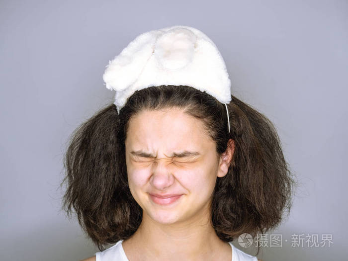 一个戴着白兔耳朵的年轻女人眯着眼睛在灰色背景下孤立