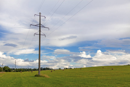 一根电缆在田野里,有一根高电压电线杆,背景是森林和天空照片