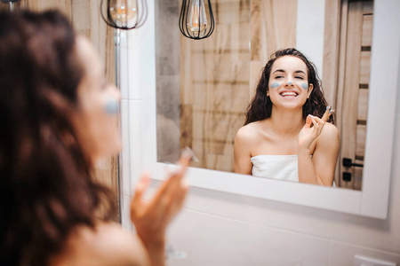 开朗快乐的模特照镜子微笑.她在脸上和鼻子上抹了些奶油.照片