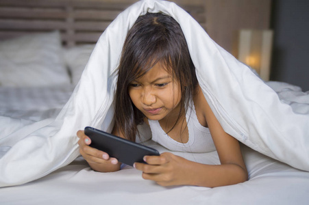 床网快乐美丽的7岁孩子在床上玩手机玩网络游戏,在年轻女孩和科技概念