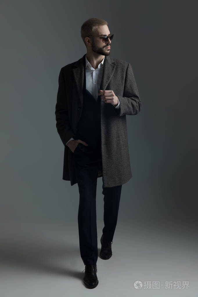 穿着西装戴着墨镜穿着长外套散步的金发男子