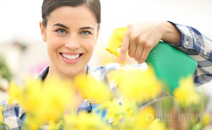 微笑的女人在花园里喷洒花草，春天的概念