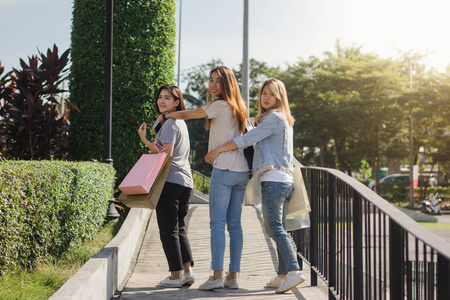 年轻的亚洲女性在温暖的阳光下展示她们购物袋里的东西.