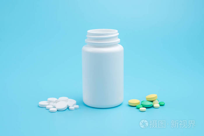 White, yellow and green pills, tablets and white bottle on blue 