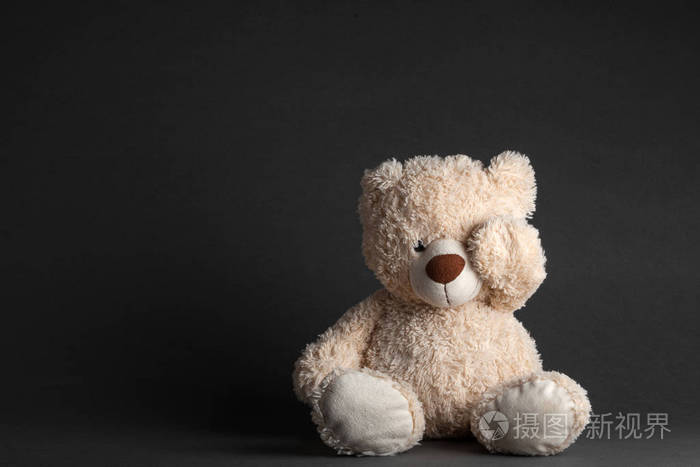 一只小熊坐在一间黑屋的椅子上,两手紧闭着眼睛