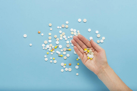 女性手拿着一颗药丸在蓝色背景上的手掌上,上面有散落的药丸.