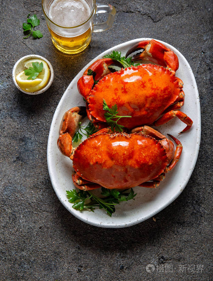 白盘子里的全熟螃蟹柠檬和啤酒灰色混凝土背景俯视图