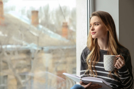 美丽的年轻女子坐在窗台上看书喝咖啡年轻时尚的女人看书在图书馆看书