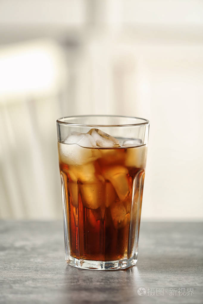 在模糊的背景下桌上放着一杯可乐和冰块为文字留出空间
