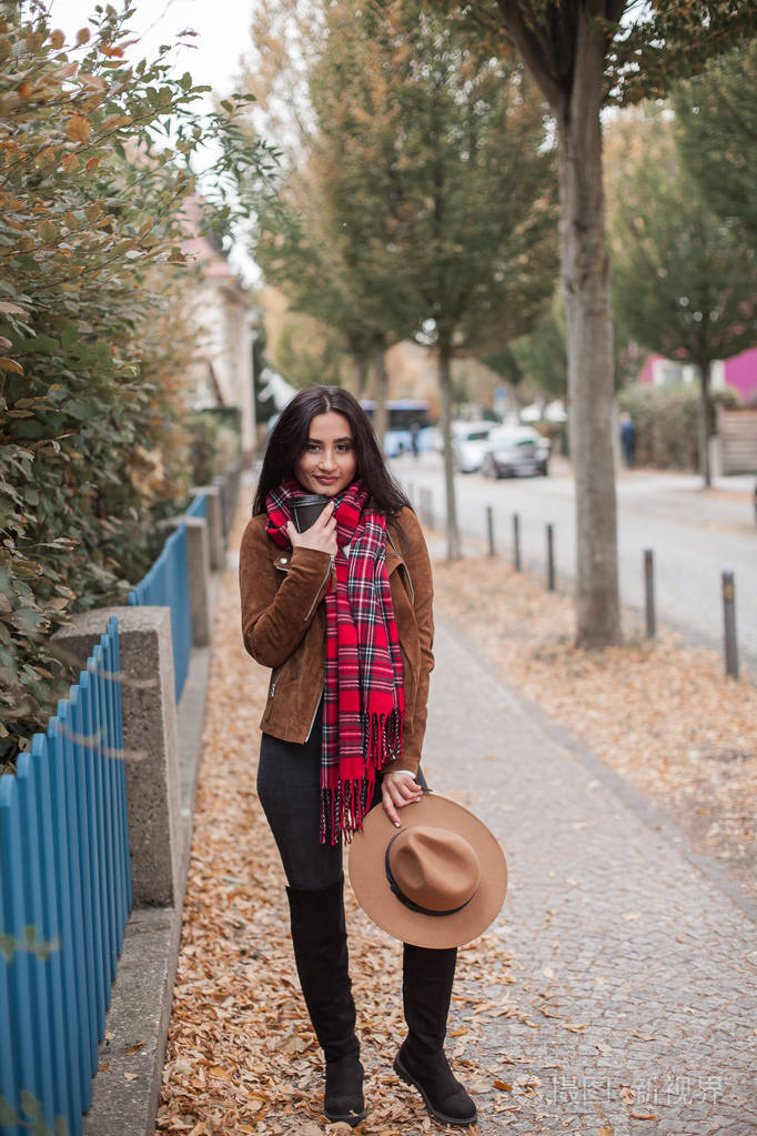 一位美丽的年轻女子走在欧洲的一座城市里,手里拿着一顶帽子,喝着咖啡