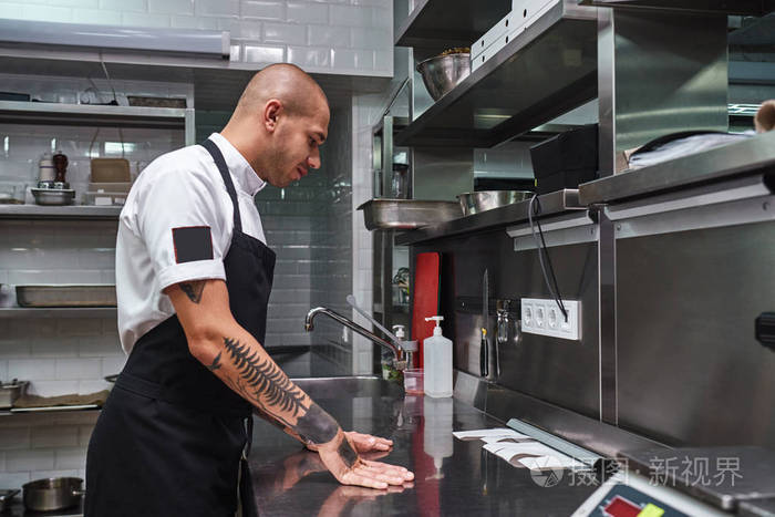 我们开始吧年轻的秃顶男厨师手臂上有美丽的纹身他看着餐厅厨房的钢