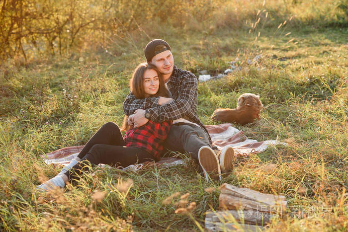 年轻人温柔地拥抱他漂亮的女朋友日落时分这对年轻夫妇坐在绿色草坪上