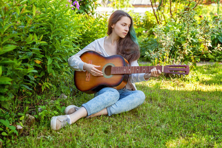 年轻女子坐在草地上弹吉他图片