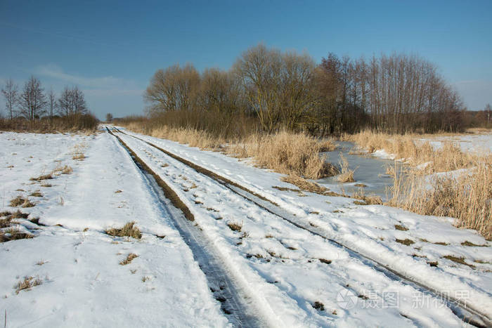 在一条土路上融化的雪穿过一片荒野的草地灌木丛和一个c