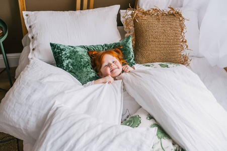 可爱快乐的红发女孩躺在家里的床上.俯视图照片