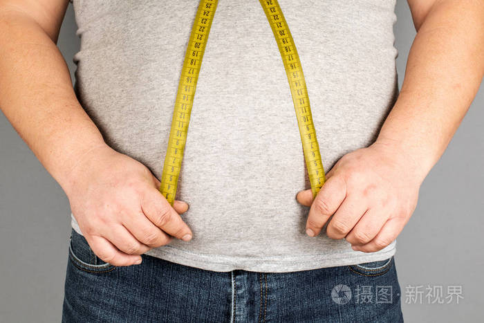 一个男人用卷尺量他的胖肚子在灰色的ba上