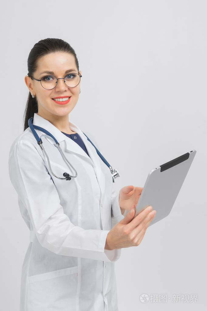 身着医生服装的深色头发的肖像，手上拿着一块现代平板电脑，背景是孤立的