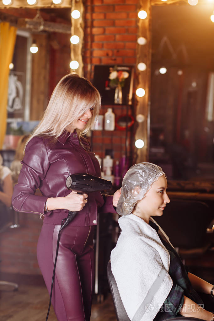 笑容可掬的专业美发师与女客户在美发厅手持专业吹风机一起工作美与人