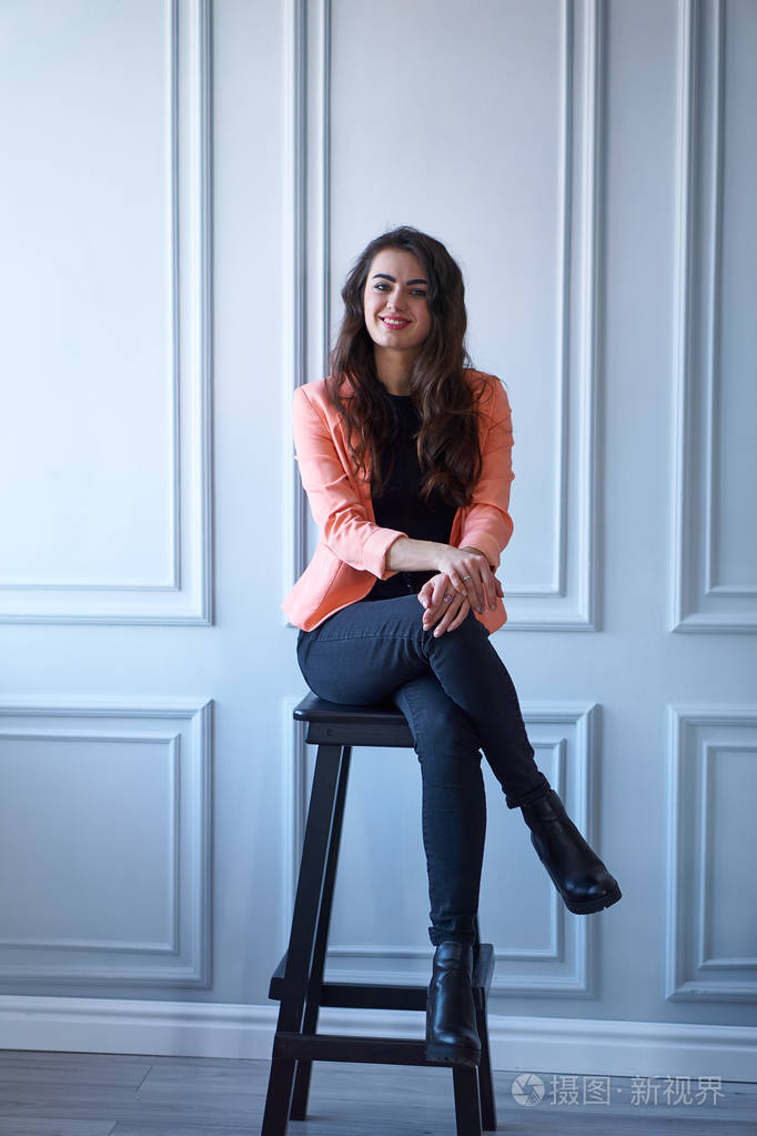 一个穿着桃红色夹克坐在椅子上的迷人的黑发女孩的肖像