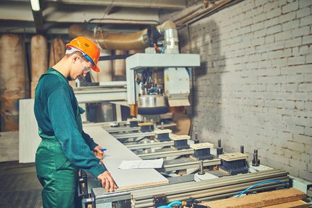 工厂里操作计算机控制机器的工人照片