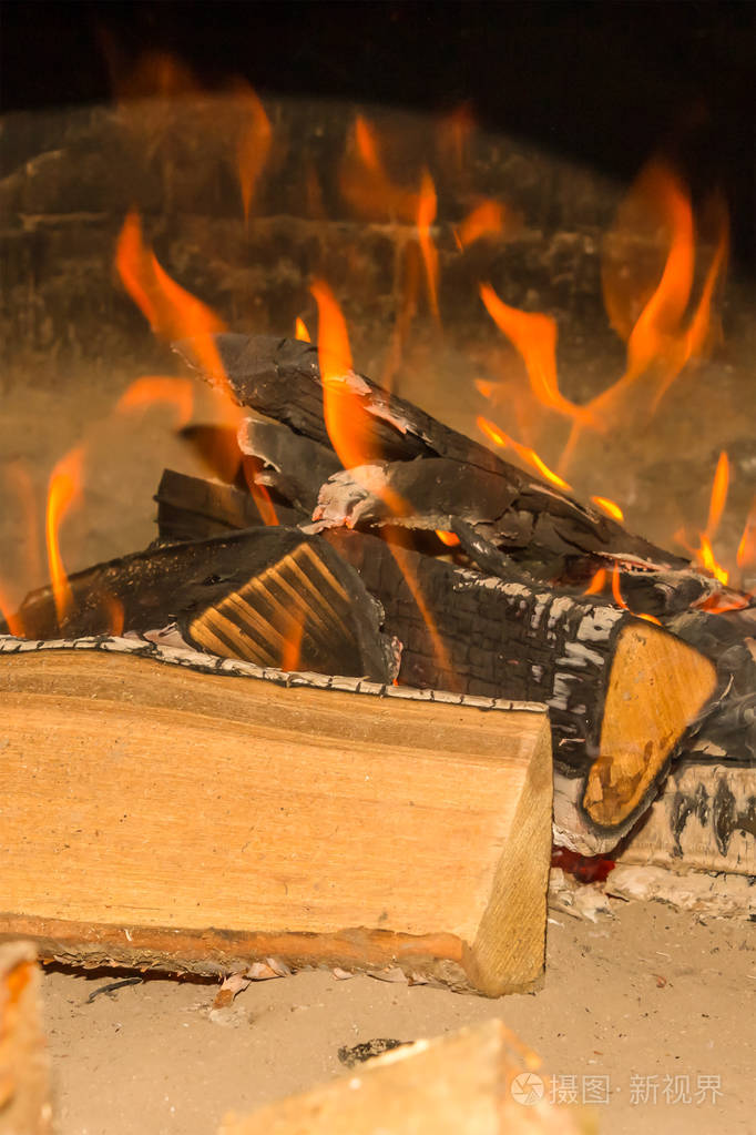 篝火明亮的橙色火焰大圆木燃烧覆盖着沙子上的灰烬特写