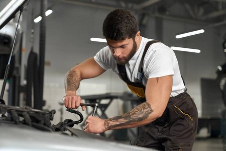 穿着工作服的肌肉发达的机械师,白色t恤在修车.照片