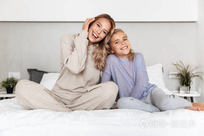 快乐的女孩姐妹们在家卧室的床上摆出微笑。