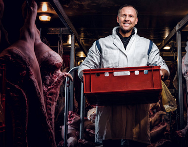 穿着工作服的愉快的屠夫,手里拿着一个装着肉块的盒子,放在肉块中间