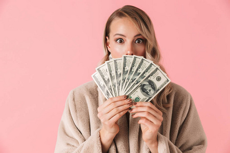一个年轻漂亮的女人拿着钱在粉红色的墙上摆着孤立的姿势.照片