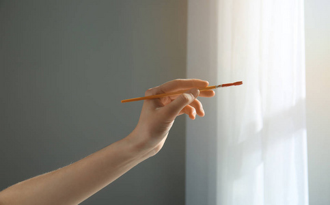 女画家手拿画笔靠近窗户照片