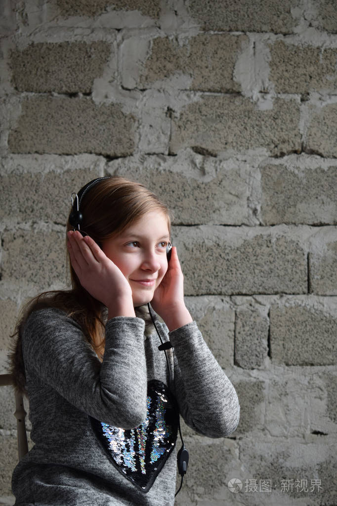 一个愉快友好快乐的少年戴着耳机听音乐的概念肖像年轻的女孩穿着一件