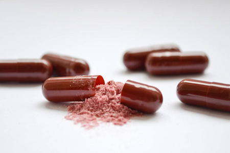 棕色药片,明胶胶囊,其中一个是开着的,里面有倒粉红色粉末的特写镜头