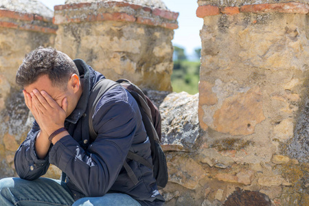 悲伤夹克一个悲伤的男人,穿着夹克,背着背包,手放在脸上,坐着照片