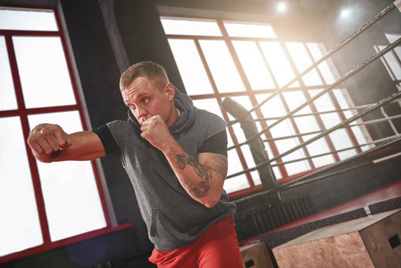 自信帅气的运动员穿着运动服在拳击台对面投掷勾拳照片