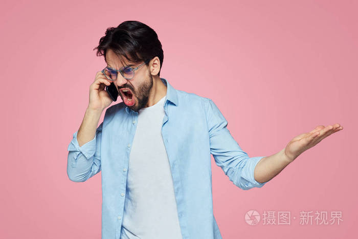 愤怒的愤怒的男人用恼怒的表情做手势在手机通话时大声尖叫在粉红色的