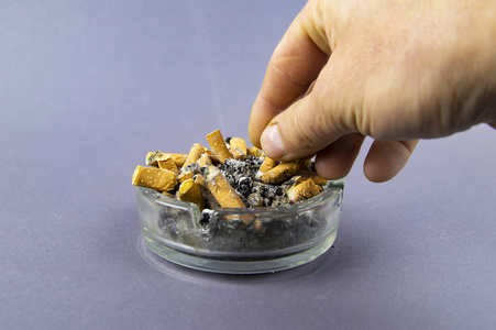 一个男人的手把香烟里的烟灰弹到满溢的烟灰缸里照片