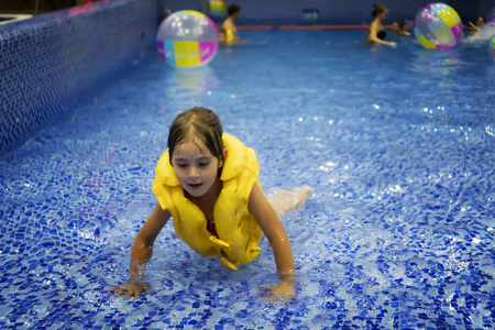 一个穿着黄色救生衣的小女孩在游泳池里游泳